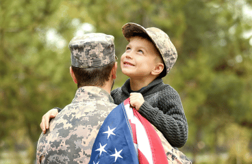 Ultimate Guide to Servicemembers' Group Life Insurance (SGLI) Featured Image. Soldier wearing camo reunited with his son. Holding his 5 y.o. son in his arms, the son holds an american flag.